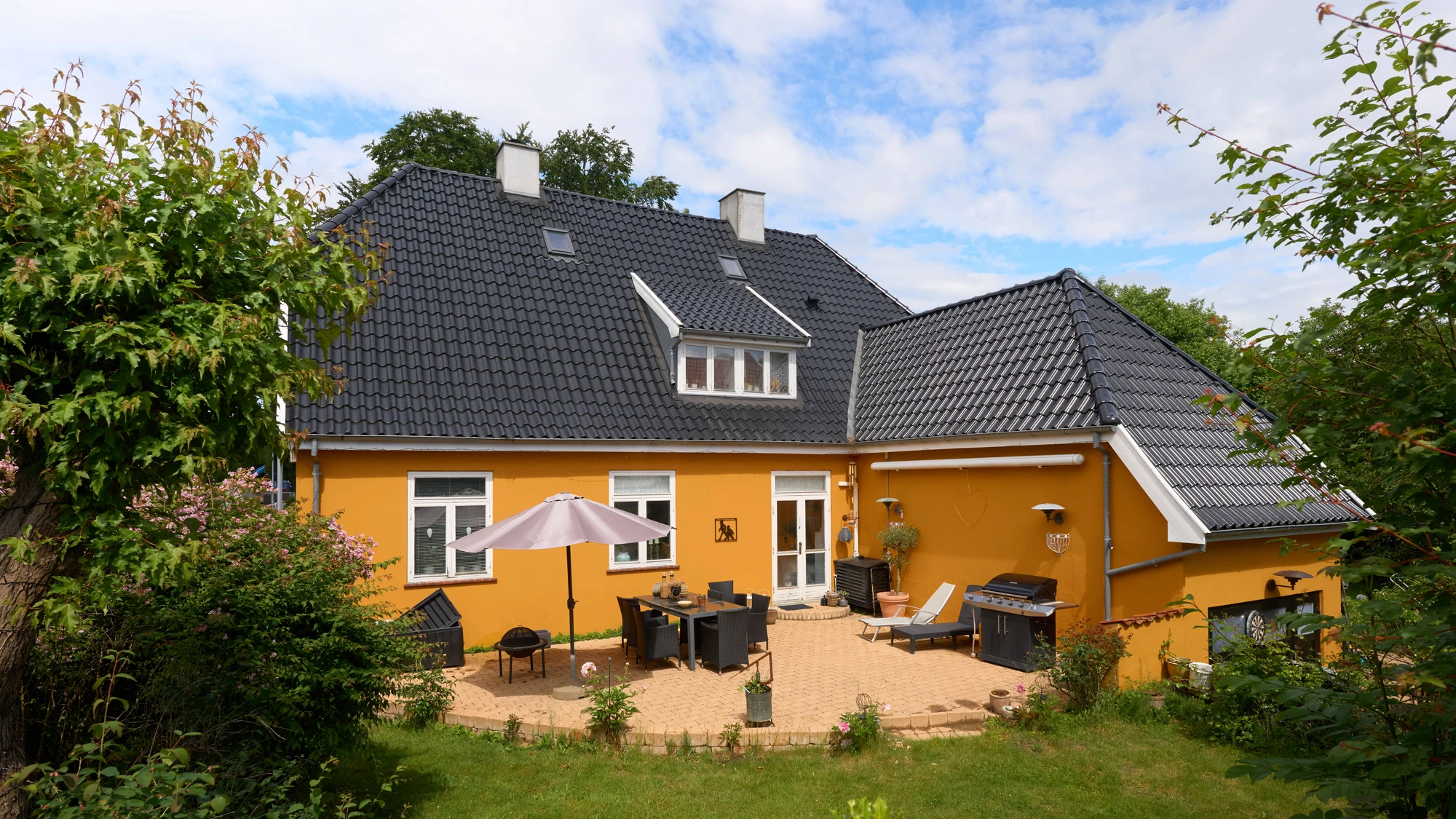 Havefacaden med sort tegltag, terrasse og frodig have