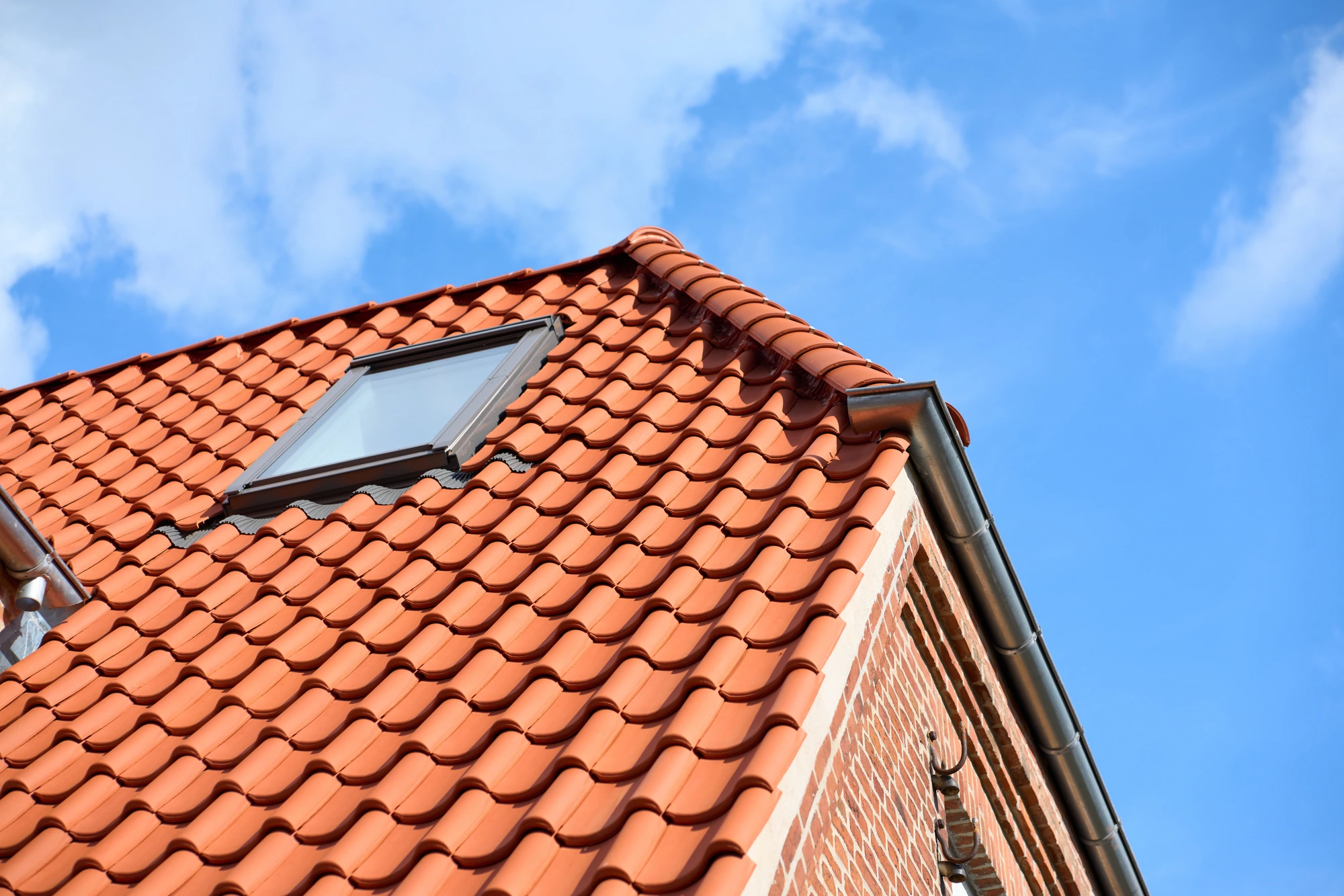 Detalje af tagryg, vingetegl og murstensgavl mod blå himmel