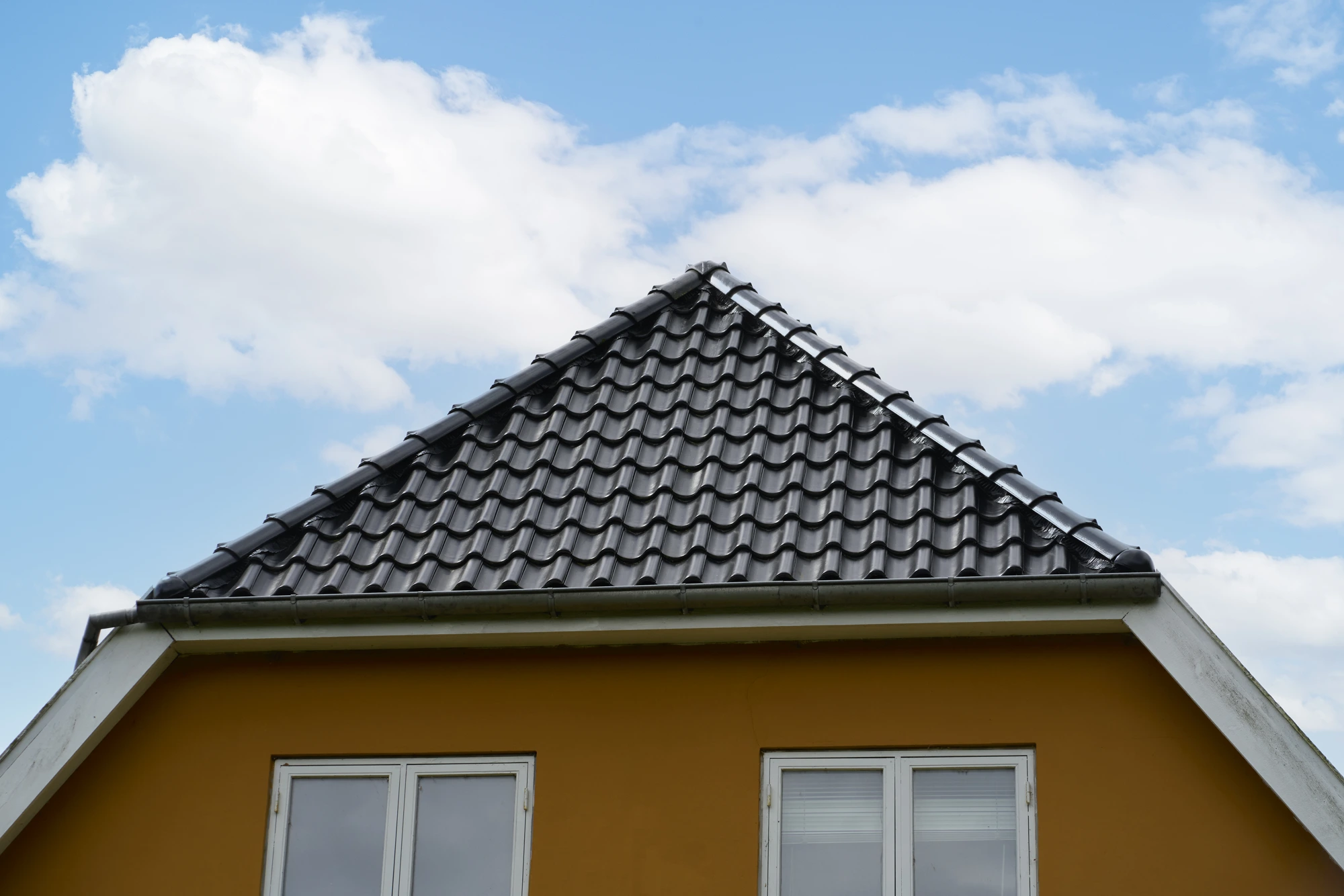Gavlspids med skorsten og sort tegltag mod blå himmel