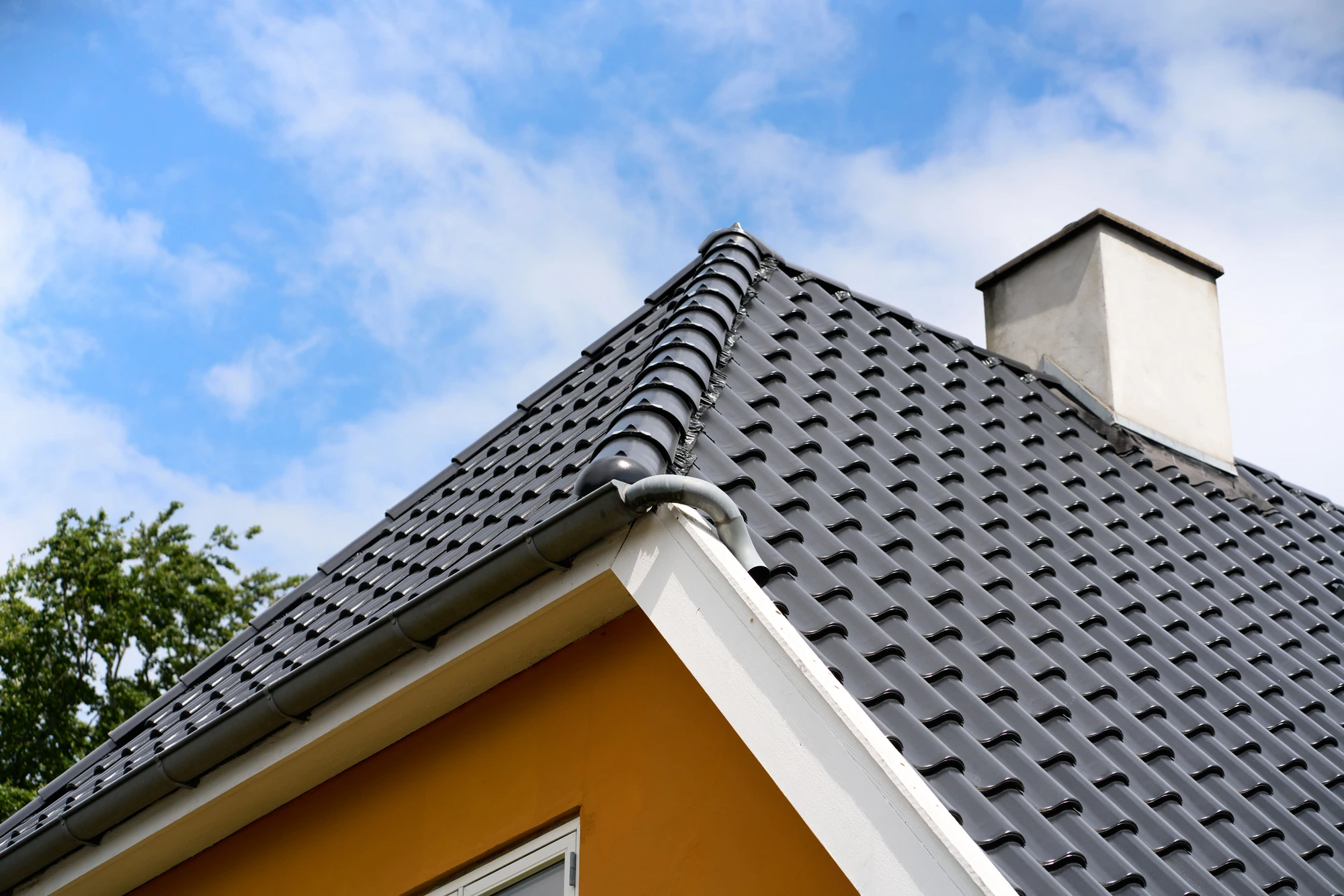 Gavl med skorsten og sort tegltag mod skyet himmel
